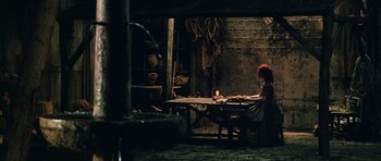 Movie still from “Perfume: The Story of a Murderer” (2006), directed by Tom Tykwer – A woman sitting at a table in a dark room; Wide shot, High angle