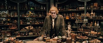 Movie still from “Perfume: The Story of a Murderer” (2006), directed by Tom Tykwer – A man sitting at a table in a room filled with bottles; Medium shot, Low angle