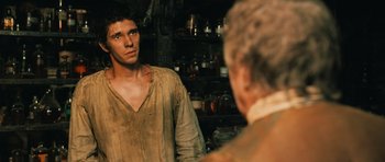 Movie still from “Perfume: The Story of a Murderer” (2006), directed by Tom Tykwer – A young man looking into a mirror while standing next to an older man; Medium shot, Over the shoulder angle