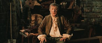 Movie still from “Perfume: The Story of a Murderer” (2006), directed by Tom Tykwer – An older man sitting in front of a pile of clothes; Medium shot, Low angle