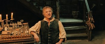 Movie still from “Perfume: The Story of a Murderer” (2006), directed by Tom Tykwer – A man wearing a green vest standing in front of stairs; Medium shot, Low angle