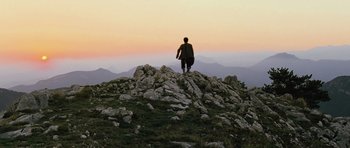Movie still from “Perfume: The Story of a Murderer” (2006), directed by Tom Tykwer – A man standing on top of a mountain holding a surfboard; Extreme Wide shot, Low angle