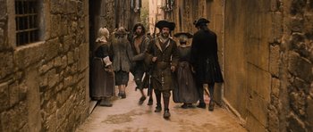 Movie still from “Perfume: The Story of a Murderer” (2006), directed by Tom Tykwer – A group of people dressed in costumes walking down a street; Wide shot, High angle