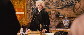 Movie still from “Perfume: The Story of a Murderer” (2006), directed by Tom Tykwer – A man in a black suit standing in front of a desk; Medium shot, High angle