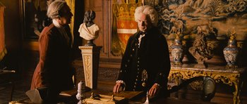 Movie still from “Perfume: The Story of a Murderer” (2006), directed by Tom Tykwer – A man in a wig and wig stands in front of a statue; Medium shot, High angle