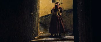 Movie still from “Perfume: The Story of a Murderer” (2006), directed by Tom Tykwer – A woman standing on some steps holding a camera; Wide shot, Low angle