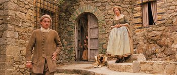 Movie still from “Perfume: The Story of a Murderer” (2006), directed by Tom Tykwer – A man and a woman and a dog in front of a stone building; Wide shot, Low angle