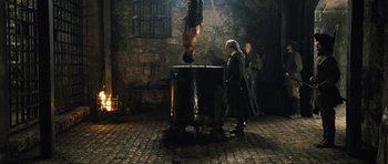 Movie still from “Perfume: The Story of a Murderer” (2006), directed by Tom Tykwer – A man hanging upside down in the middle of a room while another man looks on; Wide shot, High angle