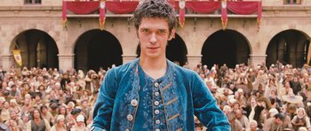 Movie still from “Perfume: The Story of a Murderer” (2006), directed by Tom Tykwer – A young man in a blue outfit standing in front of a crowd; Medium shot, Low angle