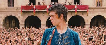 Movie still from “Perfume: The Story of a Murderer” (2006), directed by Tom Tykwer – A man in a blue jacket standing in front of a crowd of people; Medium shot, Low angle