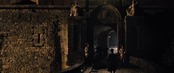 Movie still from “Perfume: The Story of a Murderer” (2006), directed by Tom Tykwer – A group of people standing in front of an archway in the dark; Extreme Wide shot, High angle