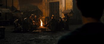 Movie still from “Perfume: The Story of a Murderer” (2006), directed by Tom Tykwer – A group of people sitting around a fire pit; Wide shot, High angle