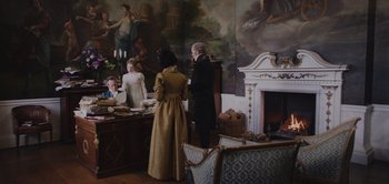 Movie still from “Persuasion” (2022), directed by Carrie Cracknell – A man and a woman standing in front of a fireplace; Wide shot, High angle