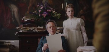 Movie still from “Persuasion” (2022), directed by Carrie Cracknell – An older man and a young woman holding papers; Medium shot, Low angle