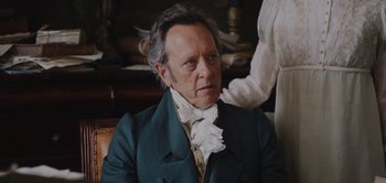 Movie still from “Persuasion” (2022), directed by Carrie Cracknell – An older man wearing a green suit and a white shirt; Close Up shot, Over the shoulder angle