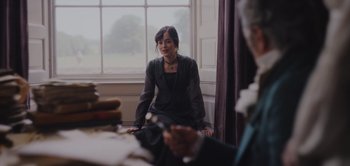 Movie still from “Persuasion” (2022), directed by Carrie Cracknell – A woman sitting in front of a large window; Medium shot, Over the shoulder angle