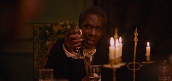 Movie still from “Persuasion” (2022), directed by Carrie Cracknell – A man sitting at a dinner table holding a wine glass; Close Up shot, Low angle