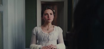Movie still from “Persuasion” (2022), directed by Carrie Cracknell – A woman in a white dress standing in a room; Medium shot, Over the shoulder angle