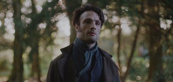 Movie still from “Persuasion” (2022), directed by Carrie Cracknell – A man in a brown jacket standing next to a tree; Close Up shot, Low angle