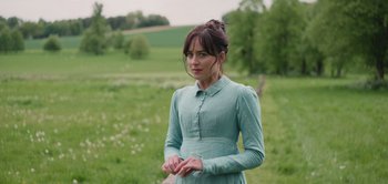 Movie still from “Persuasion” (2022), directed by Carrie Cracknell – A woman in a green dress standing in a green field; Medium shot, Over the shoulder angle