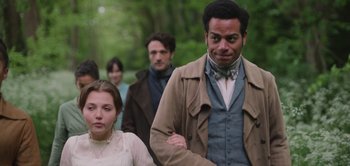 Movie still from “Persuasion” (2022), directed by Carrie Cracknell – A man and a woman walking in front of other people; Medium shot, Over the shoulder angle