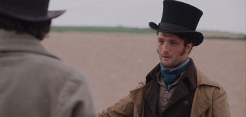 Movie still from “Persuasion” (2022), directed by Carrie Cracknell – A man wearing a top hat talking to another man in an open field; Close Up shot, Over the shoulder angle