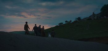 Movie still from “Persuasion” (2022), directed by Carrie Cracknell – A group of people standing on top of a green hill; Extreme Wide shot, Low angle