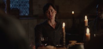 Movie still from “Persuasion” (2022), directed by Carrie Cracknell – A woman sitting in front of a lit candle and a glass of wine; Medium shot, Over the shoulder angle