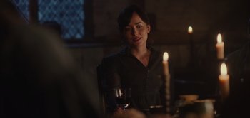 Movie still from “Persuasion” (2022), directed by Carrie Cracknell – A woman sitting at a table with a glass of red wine; Medium shot, Over the shoulder angle