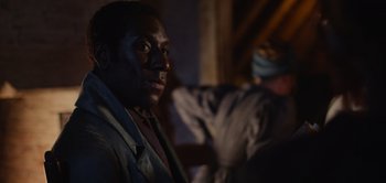 Movie still from “Persuasion” (2022), directed by Carrie Cracknell – A black man is sitting in a dark room; Close Up shot, Over the shoulder angle