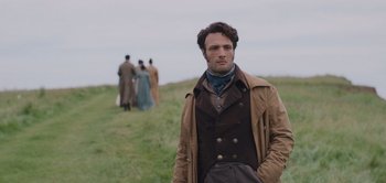 Movie still from “Persuasion” (2022), directed by Carrie Cracknell – A man standing in a field with other people in the background; Medium shot, Over the shoulder angle