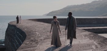 Movie still from “Persuasion” (2022), directed by Carrie Cracknell – A man and a woman walking down a beach; Wide shot, High angle