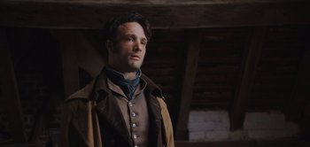 Movie still from “Persuasion” (2022), directed by Carrie Cracknell – A man in a brown and tan jacket looking to his left; Close Up shot, Over the shoulder angle