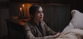 Movie still from “Persuasion” (2022), directed by Carrie Cracknell – A woman sitting at a table in front of a lit candle; Close Up shot, High angle