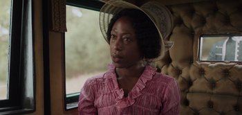 Movie still from “Persuasion” (2022), directed by Carrie Cracknell – A woman wearing a pink shirt and a straw hat; Close Up shot, Over the shoulder angle