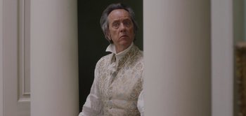 Movie still from “Persuasion” (2022), directed by Carrie Cracknell – An older man wearing a white shirt and a white vest; Close Up shot, Low angle