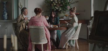 Movie still from “Persuasion” (2022), directed by Carrie Cracknell – A group of women sitting at a table with food; Wide shot, High angle