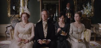 Movie still from “Persuasion” (2022), directed by Carrie Cracknell – A group of people sitting in a room holding tea cups; Medium shot, High angle