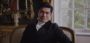 Movie still from “Persuasion” (2022), directed by Carrie Cracknell – A person sitting on a chair wearing a suit; Medium shot, Low angle