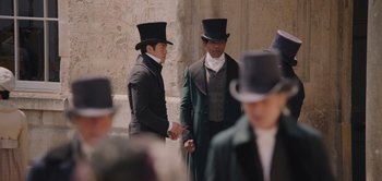 Movie still from “Persuasion” (2022), directed by Carrie Cracknell – Two men in top hats are standing next to each other; Medium shot, Over the shoulder angle