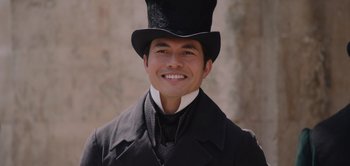 Movie still from “Persuasion” (2022), directed by Carrie Cracknell – A man wearing a top hat smiling for the camera; Close Up shot, High angle