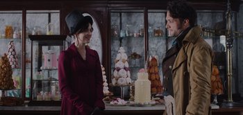 Movie still from “Persuasion” (2022), directed by Carrie Cracknell – A woman and a man standing in front of a table of desserts; Medium shot, Over the shoulder angle