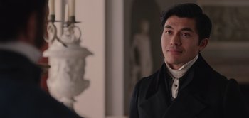 Movie still from “Persuasion” (2022), directed by Carrie Cracknell – A man wearing a black suit standing in front of a statue; Close Up shot, Over the shoulder angle