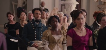 Movie still from “Persuasion” (2022), directed by Carrie Cracknell – A group of people sitting in front of a statue; Medium shot, Over the shoulder angle