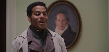 Movie still from “Persuasion” (2022), directed by Carrie Cracknell – A man standing in front of a portrait of a man; Medium shot, Low angle