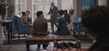 Movie still from “Persuasion” (2022), directed by Carrie Cracknell – A group of people sitting on a bench in front of a window; Wide shot, Over the shoulder angle