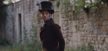 Movie still from “Persuasion” (2022), directed by Carrie Cracknell – A man wearing a top hat and a brown jacket; Medium shot, Over the shoulder angle