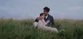 Movie still from “Persuasion” (2022), directed by Carrie Cracknell – A man and a woman sitting in the grass; Medium shot, Low angle