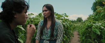Movie still from “Pet Sematary: Bloodlines” (2023), directed by Lindsey Anderson Beer – A woman in a green and blue dress standing in front of green plants; Close Up shot, Over the shoulder angle