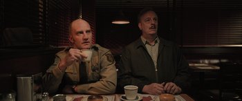 Movie still from “Pet Sematary: Bloodlines” (2023), directed by Lindsey Anderson Beer – A couple of men sitting at a table with doughnuts; Medium shot, Over the shoulder angle